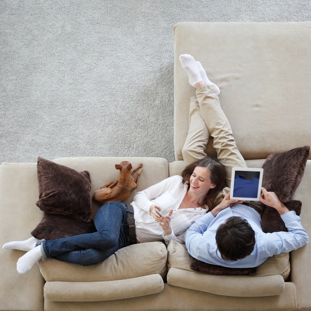 Couple se détendant sur un canapé avec leur chien, naviguant sur leurs appareils. Forfaits mobile BAYYOU