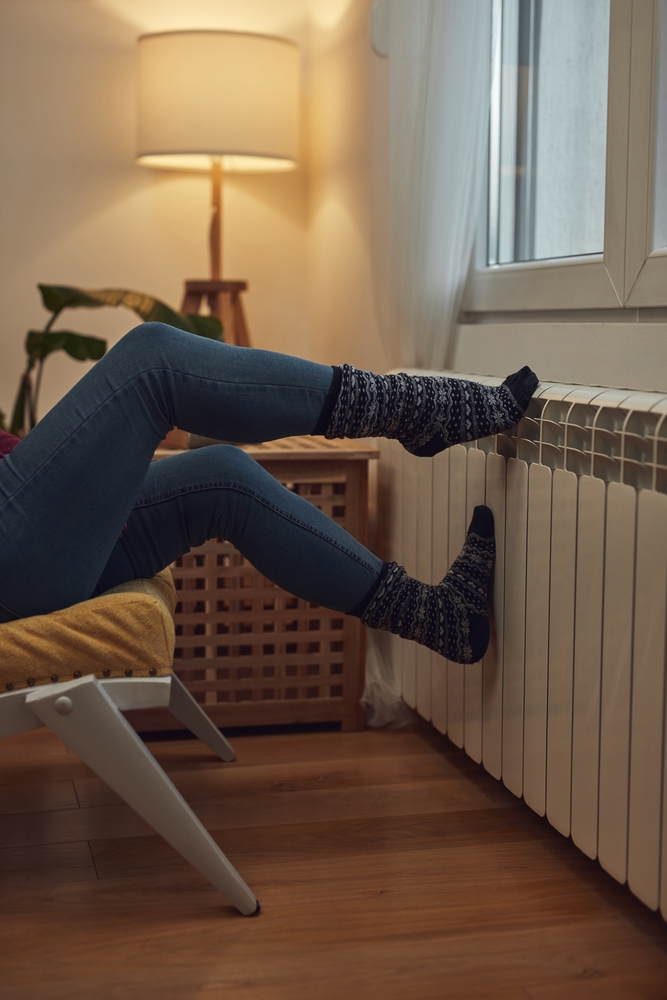 une personne en jean et chaussettes épaisses se repose les pieds sur un radiateur. Comparateur énergie de BAYYOU