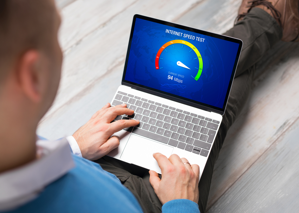 Homme effectuant un test de débit internet sur ordinateur portable affichant 94 Mbps de vitesse de connexion avant de choisir son abonnement internet.